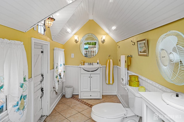 bathroom featuring a wainscoted wall, tile patterned floors, vaulted ceiling, vanity, and toilet