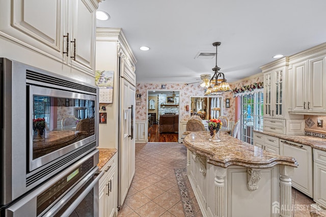 kitchen featuring wallpapered walls, a wainscoted wall, glass insert cabinets, stainless steel appliances, and light stone countertops