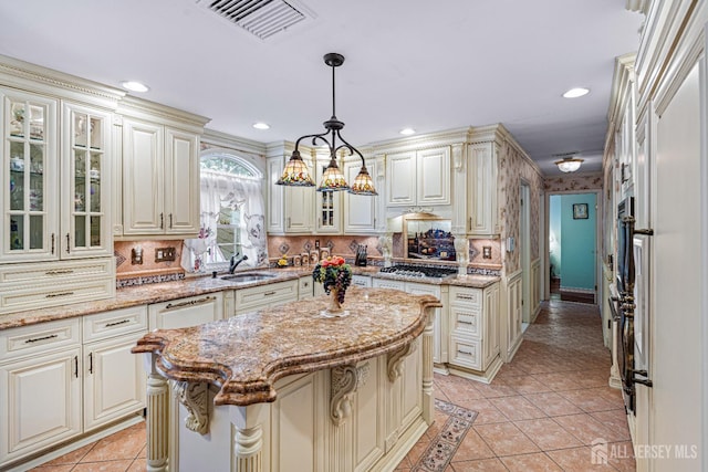 kitchen featuring stainless steel gas stovetop, a sink, cream cabinetry, light tile patterned flooring, and light stone countertops