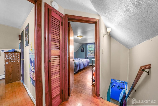 hallway featuring lofted ceiling, hardwood / wood-style flooring, a baseboard radiator, and a textured ceiling