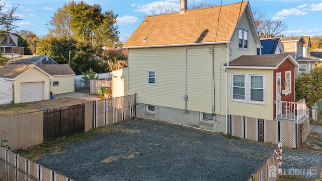 view of property exterior with a shingled roof, a detached garage, and fence