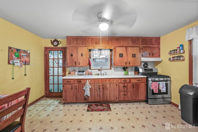 kitchen featuring gas range, brown cabinets, a sink, and light countertops