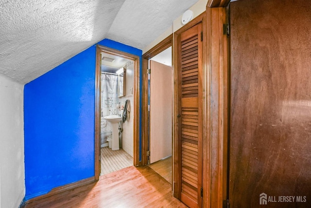 hallway with a textured ceiling, visible vents, vaulted ceiling, and wood finished floors