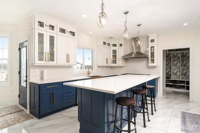 kitchen with blue cabinetry, a kitchen breakfast bar, marble finish floor, wall chimney exhaust hood, and a sink