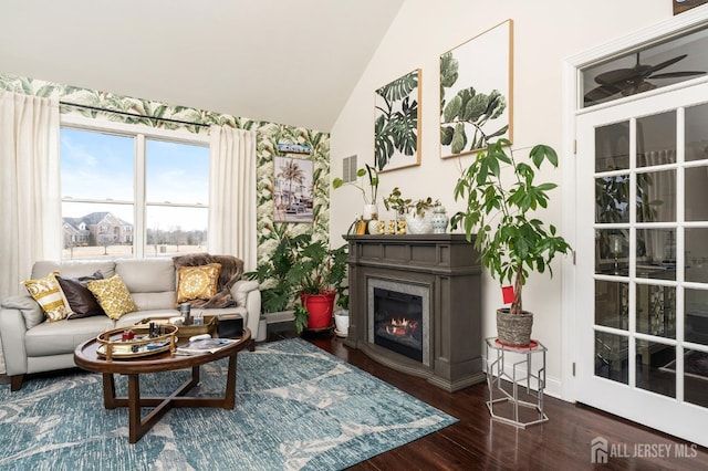 living room with a ceiling fan, wood finished floors, a glass covered fireplace, baseboards, and vaulted ceiling