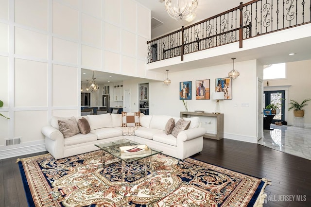 living room with visible vents, wood-type flooring, a high ceiling, baseboards, and a chandelier