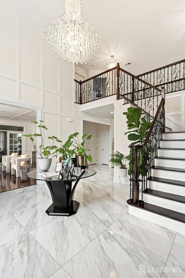 stairs with a notable chandelier, marble finish floor, and a towering ceiling