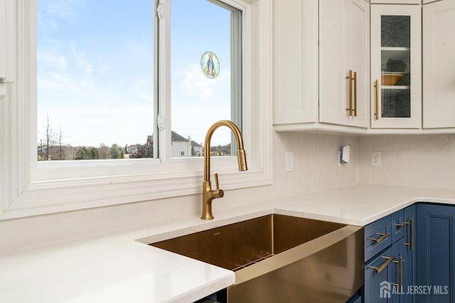 kitchen featuring blue cabinetry, glass insert cabinets, white cabinets, and a sink