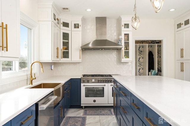 kitchen featuring blue cabinetry, appliances with stainless steel finishes, marble finish floor, wall chimney exhaust hood, and a sink