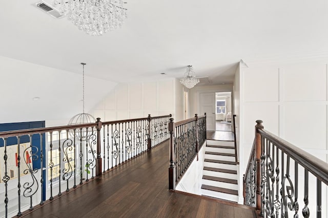 hall with wood finished floors, visible vents, an inviting chandelier, vaulted ceiling, and an upstairs landing