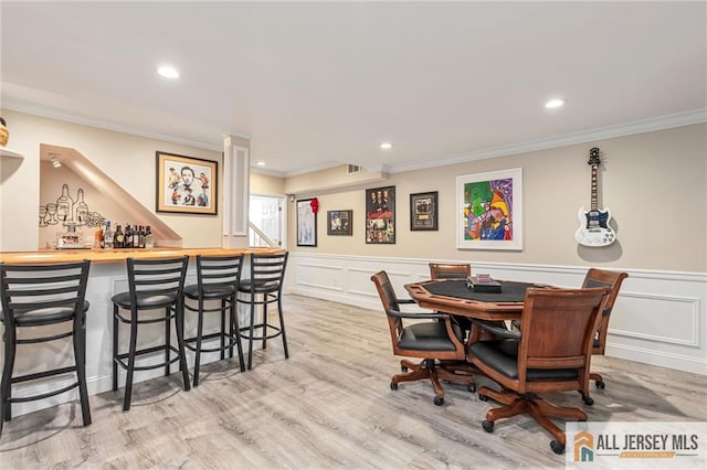 dining room with crown molding, a bar, a decorative wall, recessed lighting, and wood finished floors