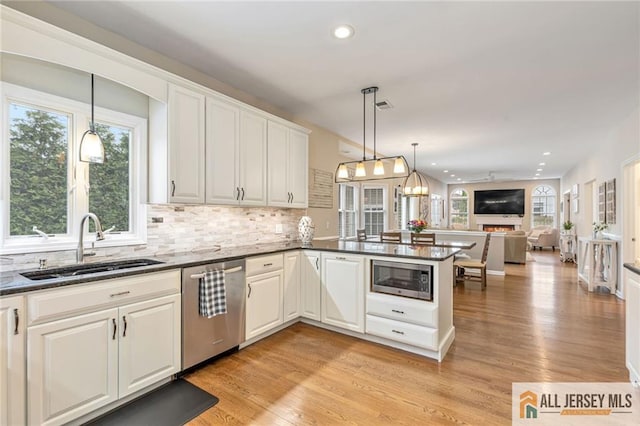kitchen with appliances with stainless steel finishes, a sink, a peninsula, backsplash, and plenty of natural light