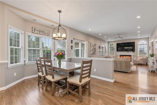 dining area with a chandelier, recessed lighting, baseboards, wood finished floors, and a lit fireplace