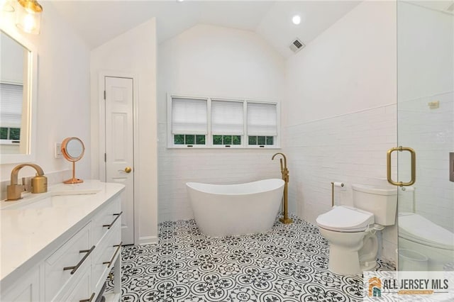 bathroom featuring toilet, a freestanding bath, lofted ceiling, vanity, and wainscoting