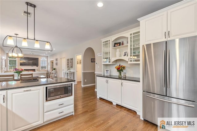 kitchen featuring stainless steel appliances, arched walkways, white cabinetry, light wood finished floors, and recessed lighting