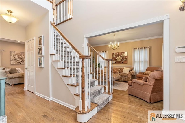 staircase with wood finished floors, crown molding, a chandelier, a high ceiling, and baseboards