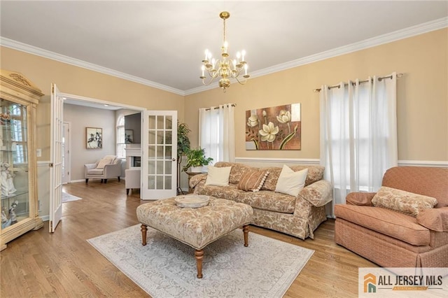 living area with french doors, a chandelier, ornamental molding, light wood finished floors, and baseboards