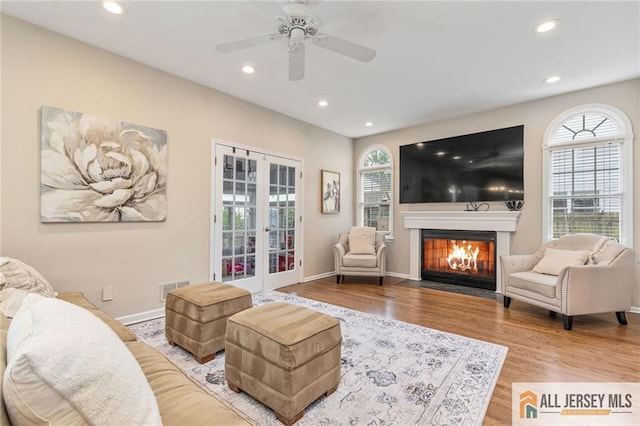 living room featuring french doors, recessed lighting, a fireplace with flush hearth, wood finished floors, and baseboards