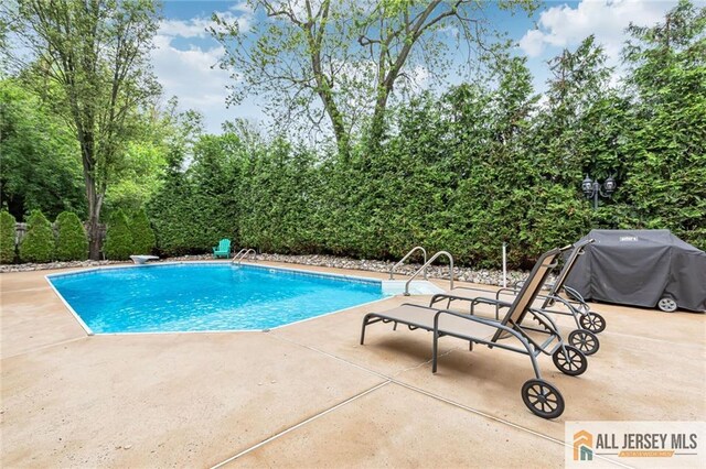 view of pool with a patio, a diving board, grilling area, and view of wooded area