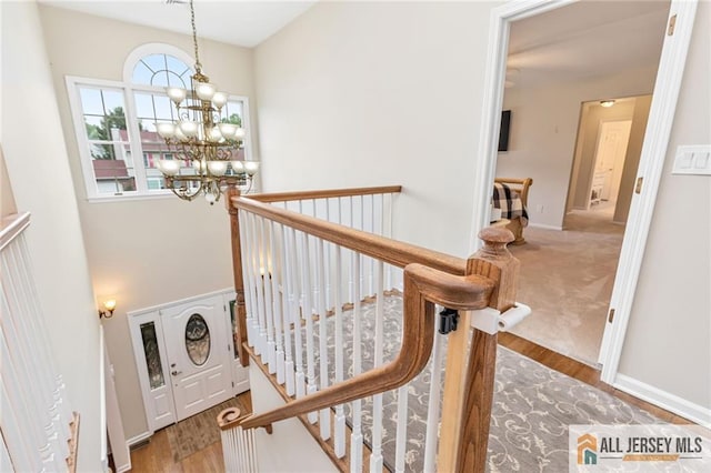 stairs with a chandelier, wood finished floors, and baseboards