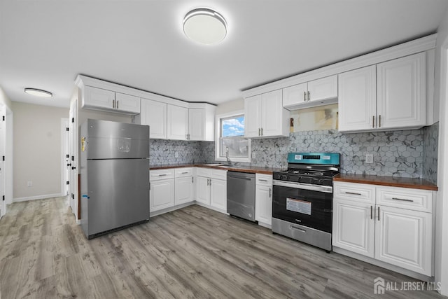 kitchen featuring appliances with stainless steel finishes, wood counters, backsplash, white cabinets, and light hardwood / wood-style floors