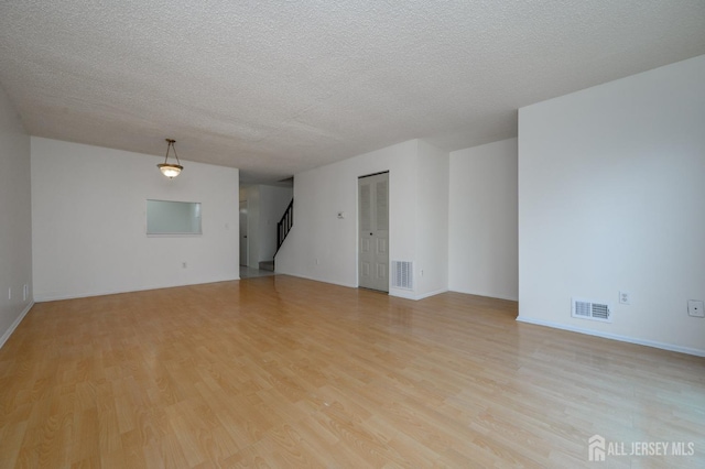 unfurnished room featuring light wood-style flooring, stairway, and visible vents