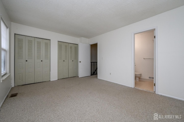 unfurnished bedroom featuring carpet floors, multiple closets, visible vents, ensuite bathroom, and a textured ceiling