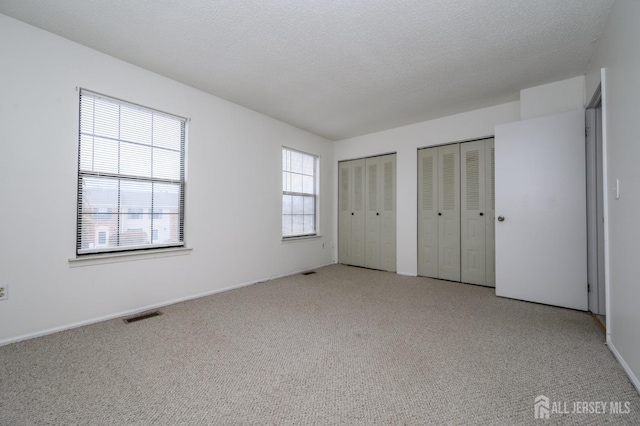 unfurnished bedroom with light carpet, a textured ceiling, two closets, and visible vents