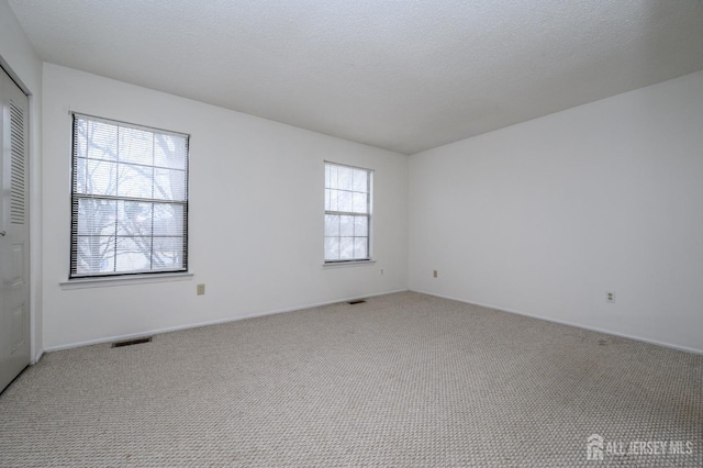 empty room with visible vents, a textured ceiling, and carpet flooring