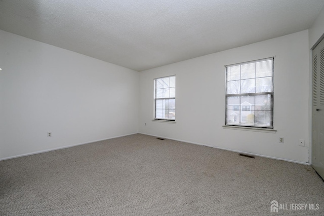 spare room featuring carpet floors, visible vents, and a textured ceiling