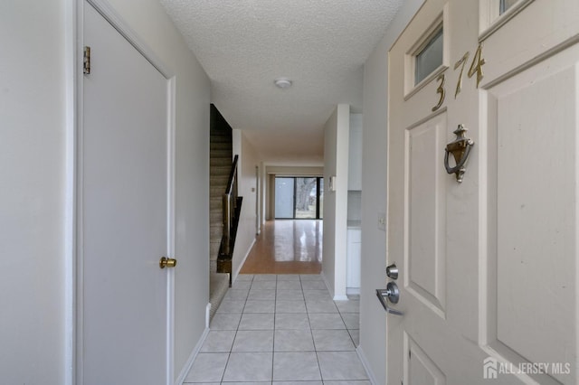 hallway with light tile patterned floors, stairs, baseboards, and a textured ceiling