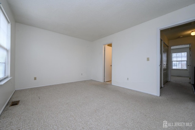 spare room featuring light carpet, baseboards, visible vents, and a textured ceiling