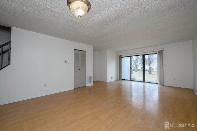 empty room with baseboards, visible vents, light wood-style flooring, and a textured ceiling