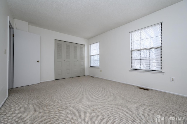 unfurnished bedroom with light colored carpet, a closet, visible vents, and a textured ceiling