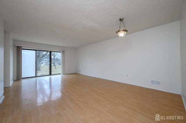 spare room with a textured ceiling, light wood finished floors, visible vents, and baseboards