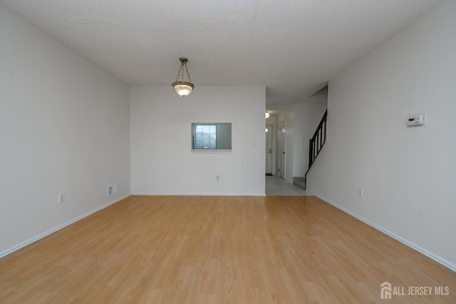 empty room featuring light wood-style flooring, visible vents, stairway, and a textured ceiling