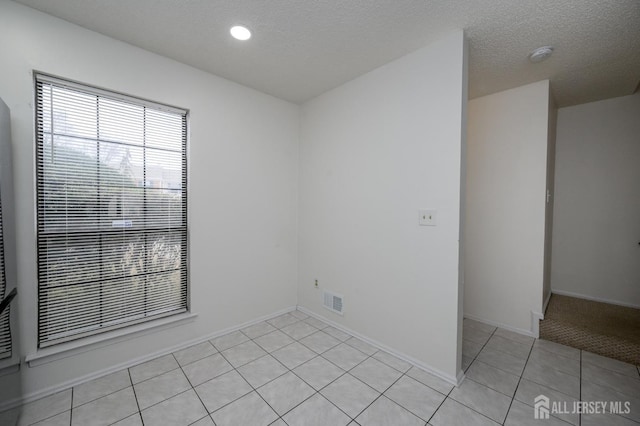 unfurnished room with light tile patterned floors, a textured ceiling, visible vents, and baseboards