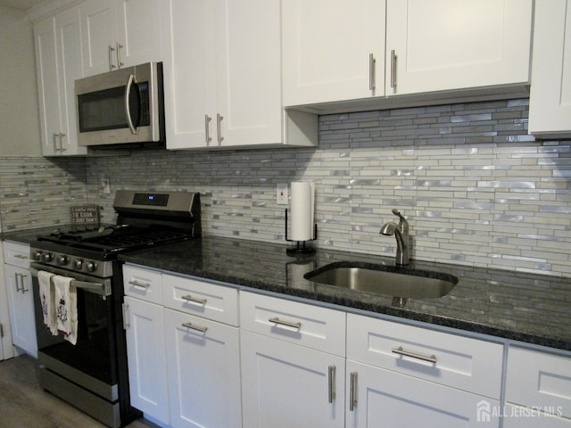 kitchen featuring appliances with stainless steel finishes, a sink, white cabinetry, backsplash, and dark stone counters