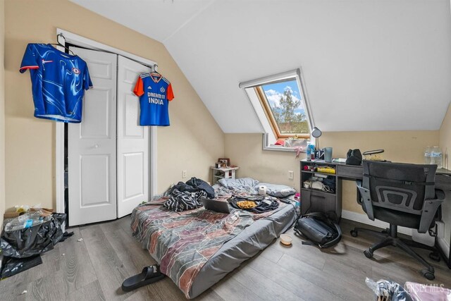 bedroom with hardwood / wood-style flooring, vaulted ceiling with skylight, and a closet