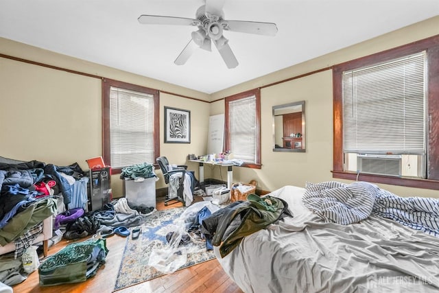 bedroom with cooling unit, ceiling fan, multiple windows, and hardwood / wood-style flooring