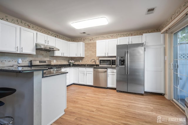 181 Windsong Cir E, Brunswick, NJ 08816 - kitchen featuring appliances with stainless steel finishes, under cabinet range hood, dark countertops, white cabinetry, and light wood finished floors