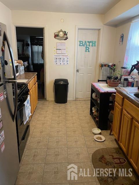 27 Edwin St, Carteret, NJ 07008 - kitchen featuring black gas range oven, light tile patterned flooring, freestanding refrigerator, and brown cabinetry