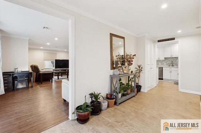 hall with light wood finished floors, ornamental molding, a sink, and recessed lighting