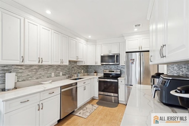 kitchen with visible vents, white cabinets, light stone counters, appliances with stainless steel finishes, and a sink