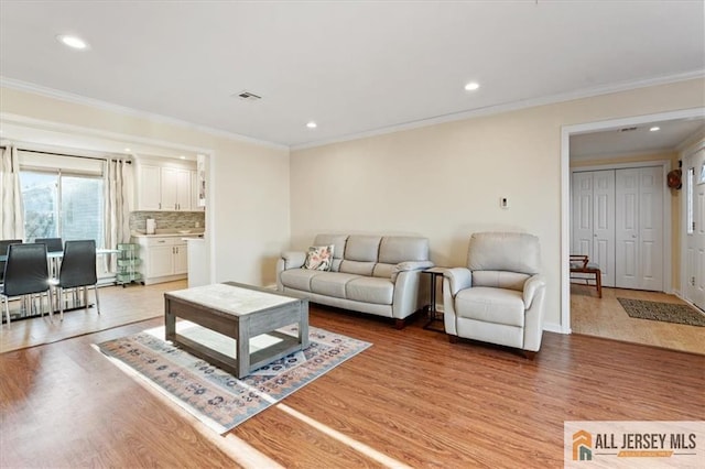 living room featuring light wood-type flooring, visible vents, crown molding, and recessed lighting