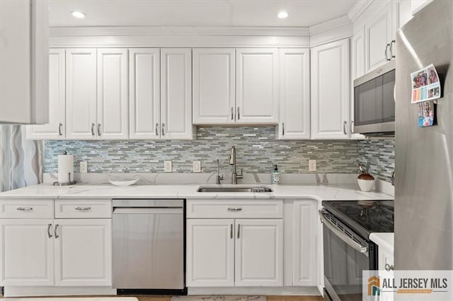 kitchen featuring stainless steel appliances, a sink, white cabinets, light stone countertops, and tasteful backsplash