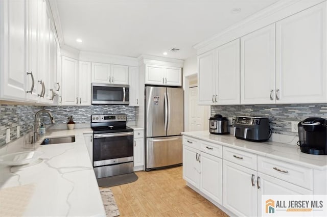 kitchen with white cabinetry, light wood-type flooring, stainless steel appliances, light stone countertops, and sink