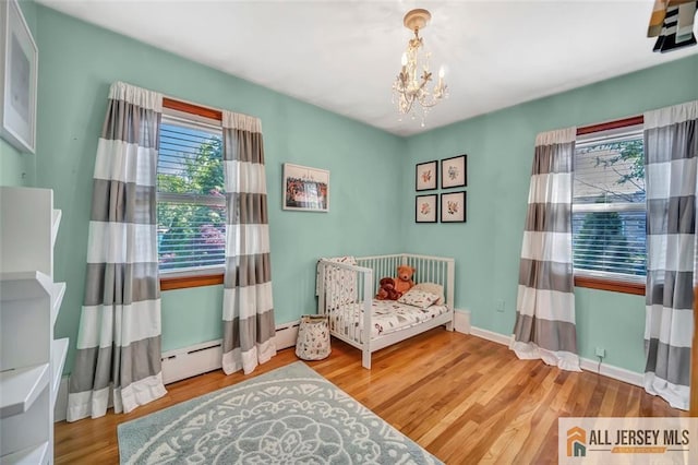living area with an inviting chandelier, plenty of natural light, wood finished floors, and a baseboard radiator
