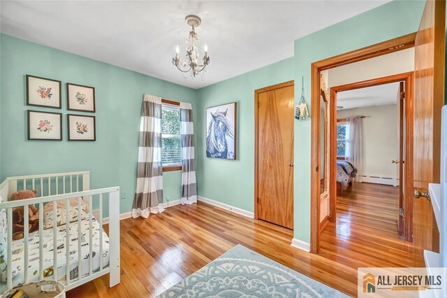 bedroom featuring an inviting chandelier, baseboards, a baseboard radiator, and wood finished floors