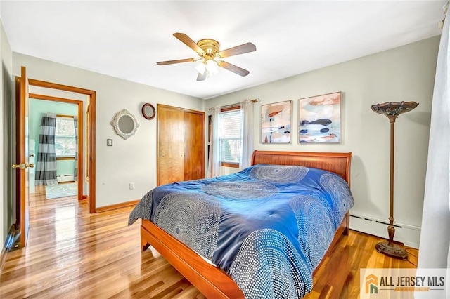 bedroom featuring a closet, baseboards, baseboard heating, and light wood-style floors
